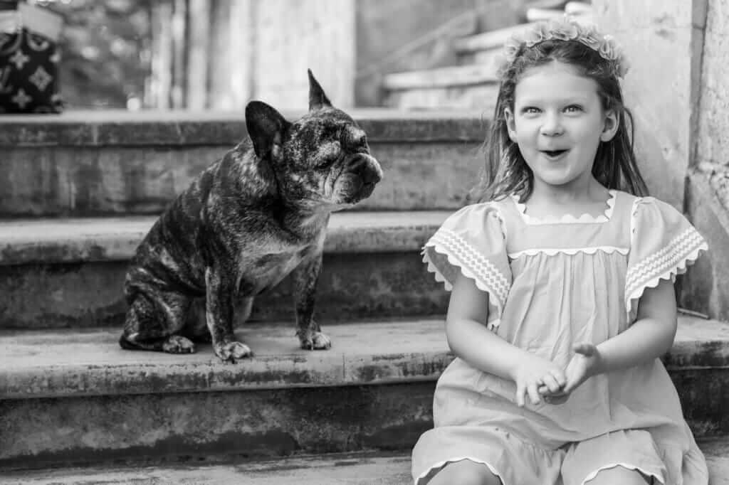 Black and white photo of a little girl laughing beside her French Bulldog during an outdoor family session in Perth.