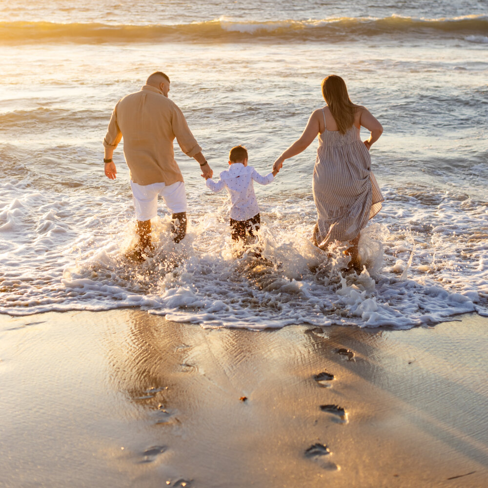 family of three running into ocean waves at sunset, beach family photography Perth
