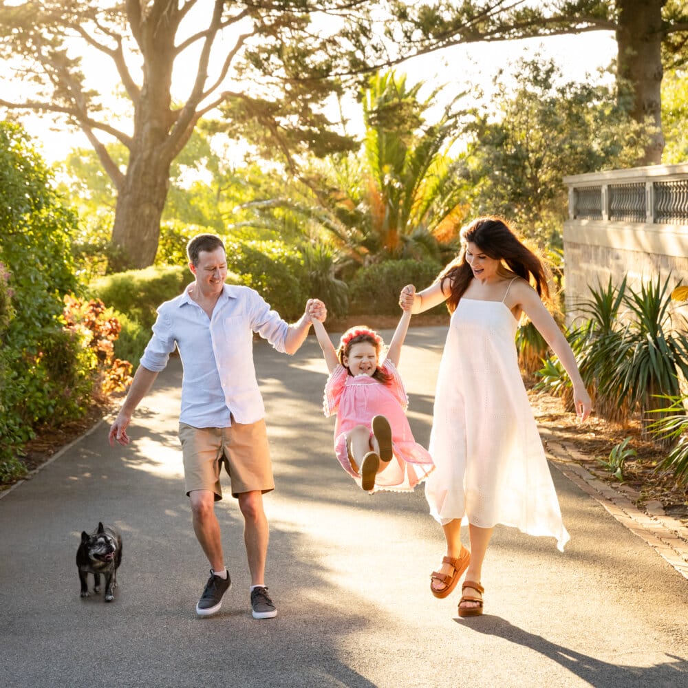 Perth family walking together in golden hour light swinging their daughter between them with their French Bulldog trotting alongside.
