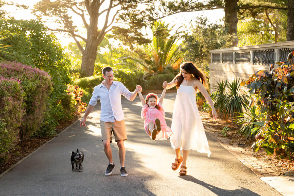 parents swinging young daughter between them in park at golden hour, family photography Perth