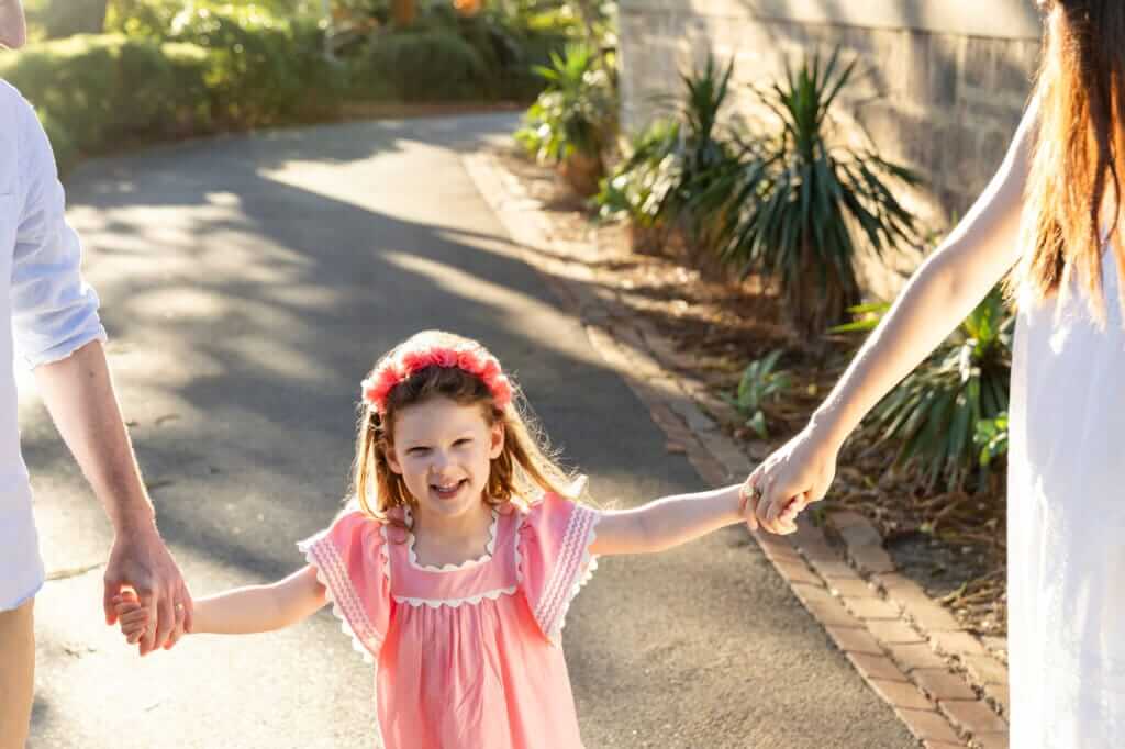 Little girl laughing and holding hands with her parents during a golden hour