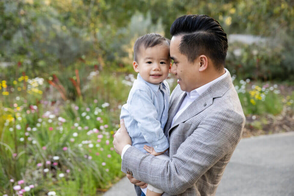 dad holding toddler son in garden among wildflowers, family photos Perth