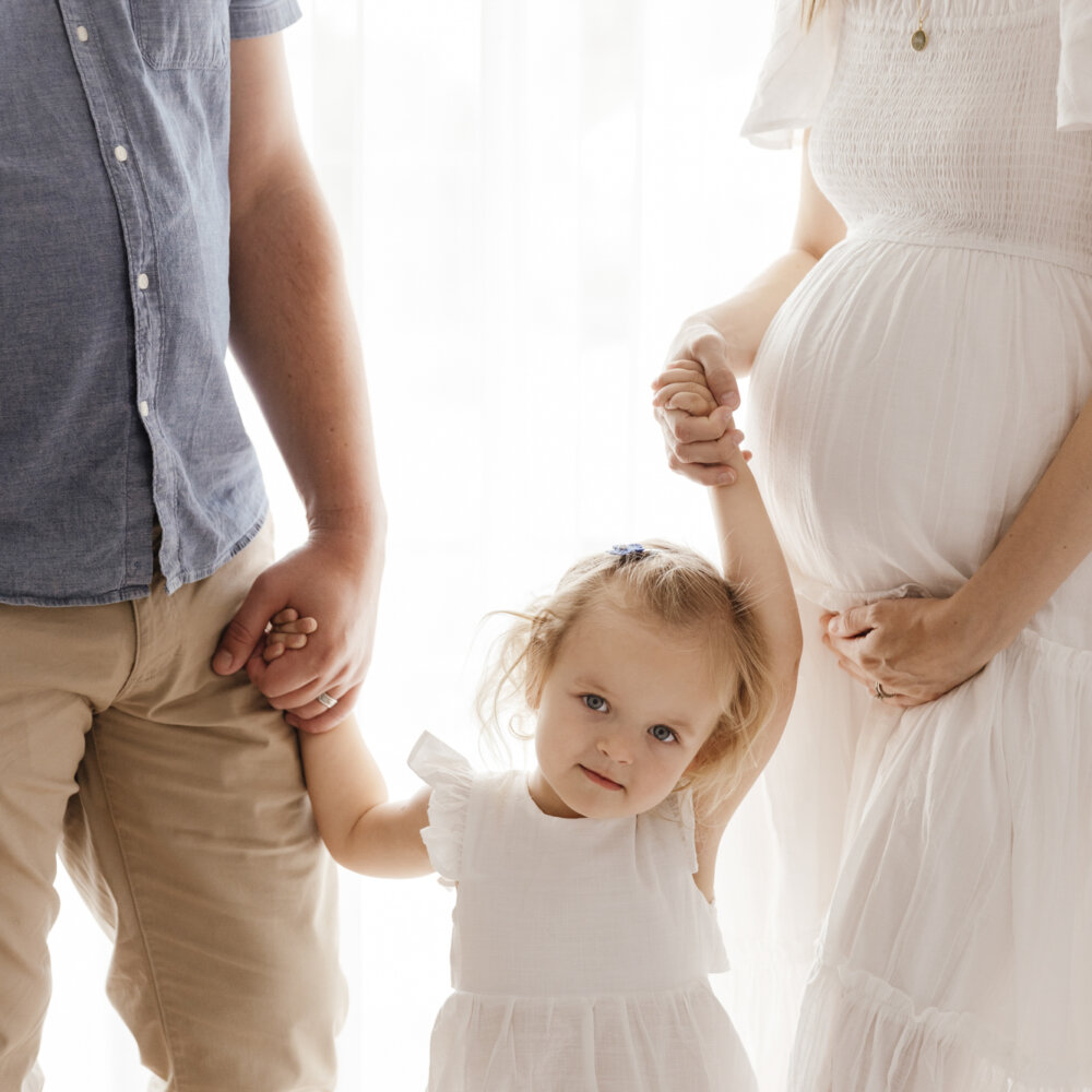 toddler girl holding hands between mum and pregnant mum in studio, maternity photography Perth