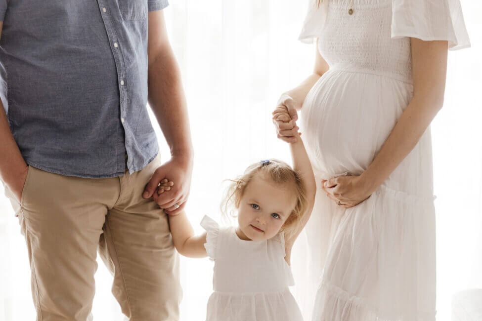 toddler girl holding hands between mum and pregnant mum in studio, maternity photography Perth