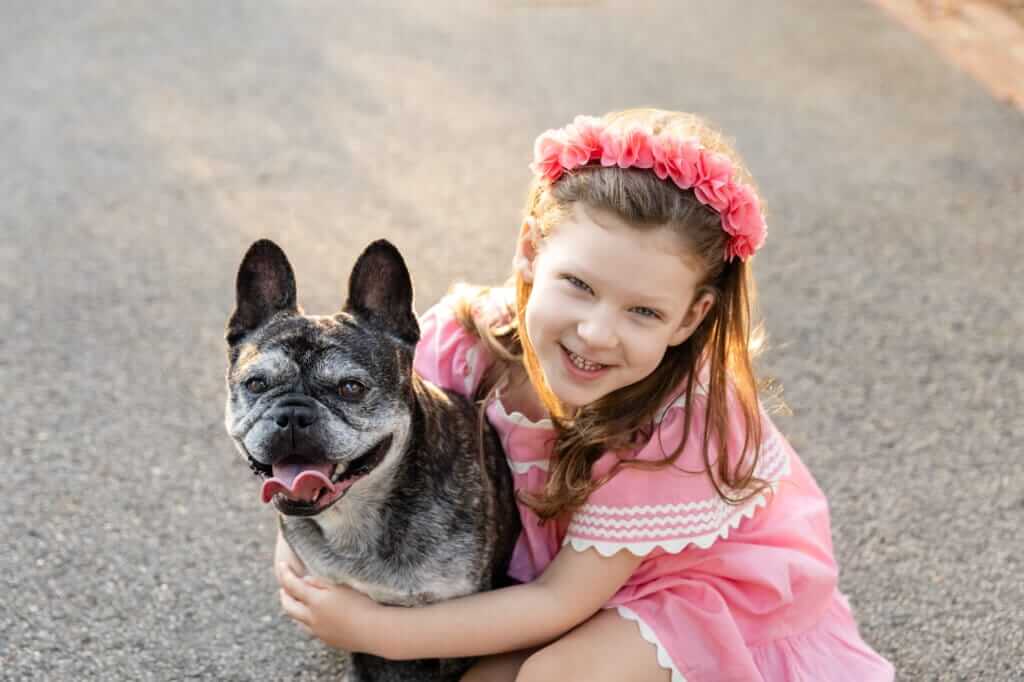 Little girl hugging her French Bulldog close and smiling at the camera during a Perth outdoor family photo shoot.