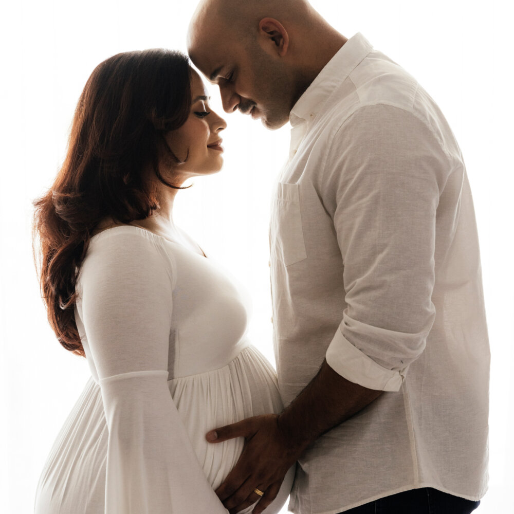 couple facing each other holding pregnant belly in studio, maternity photography Perth