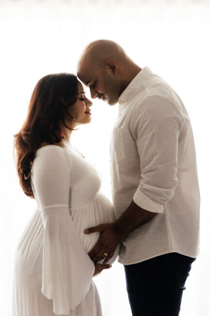 couple facing each other holding pregnant belly in studio, maternity photography Perth
