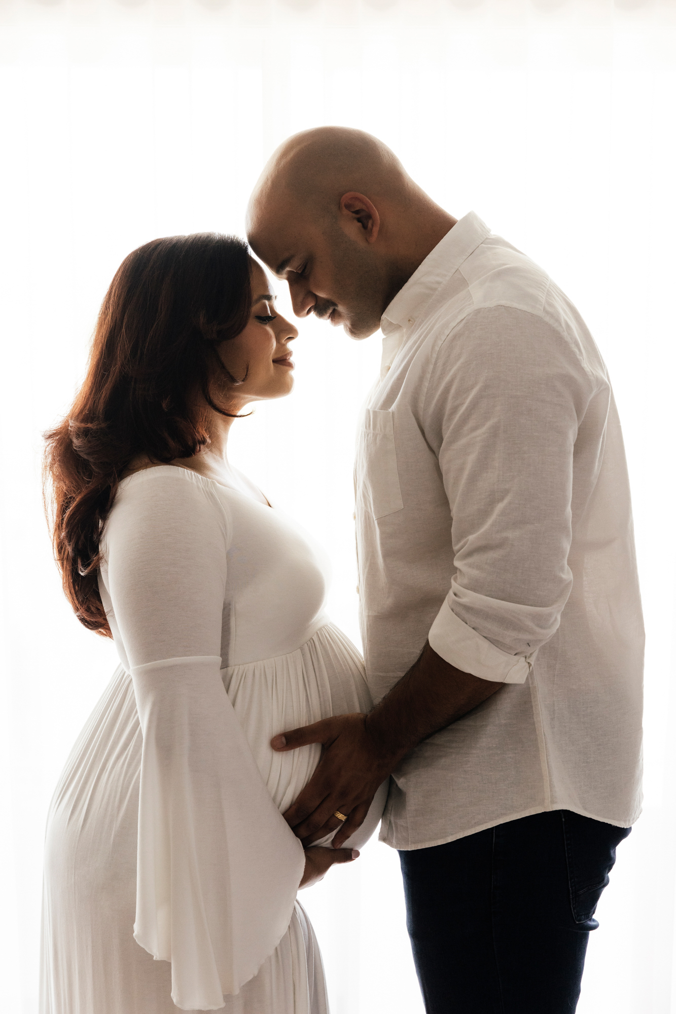 couple facing each other holding pregnant belly in studio, maternity photography Perth