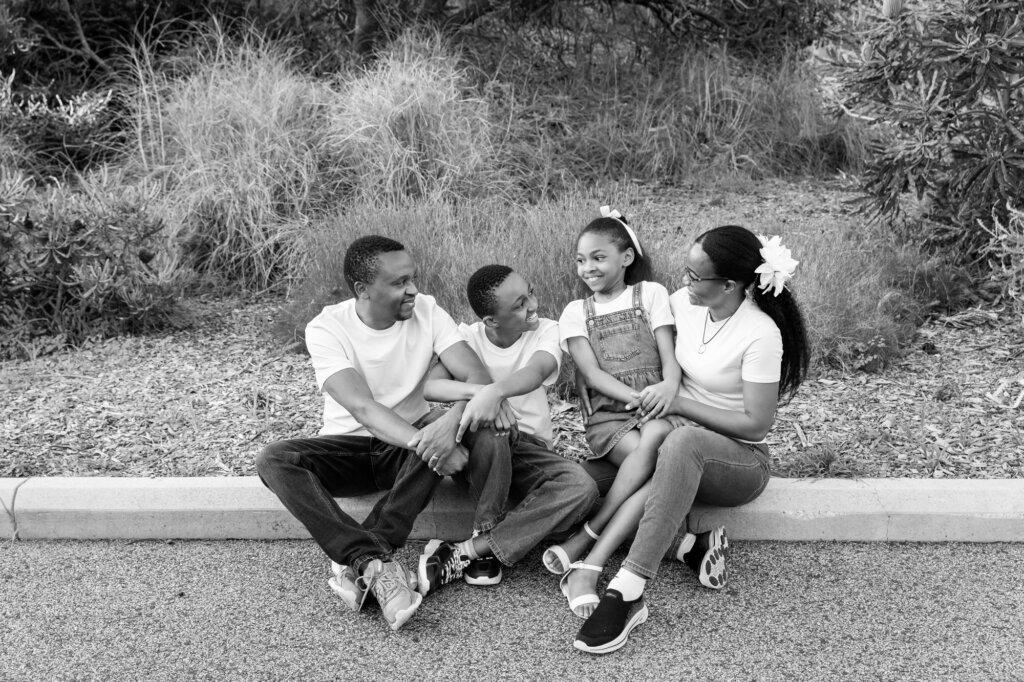 family of four sitting together on a kerb laughing and looking at each other, candid family portrait Perth
